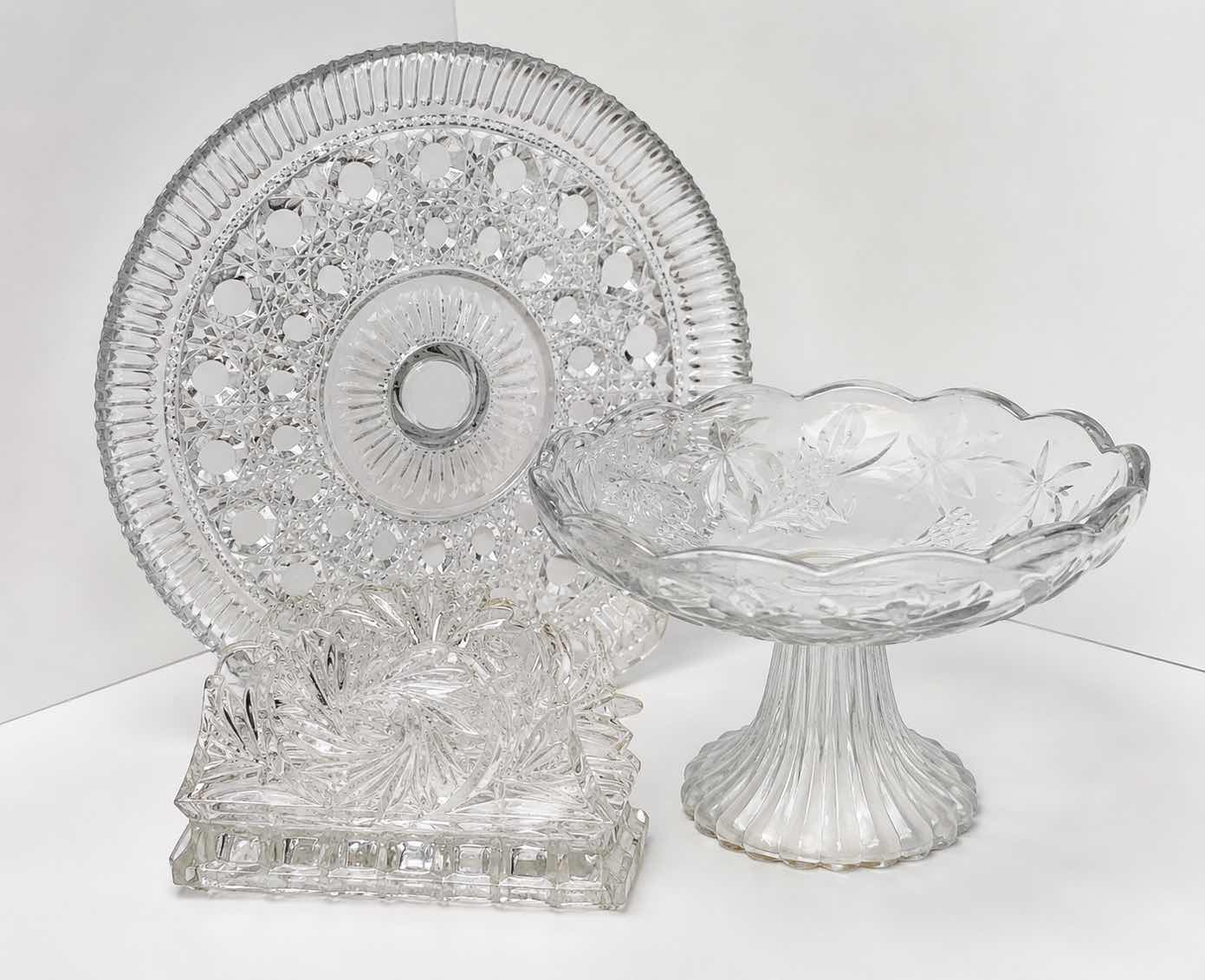Photo 1 of ASSORTED VINTAGE CLEAR PRESSED GLASS SERVING PIECES INCLUDING DECORATIVE ROUND PLATTER, PEDESTAL COMPOTE AND FLORAL RELIEF DISH.
ESTIMATED RETAIL VALUE: $40–$60 FOR THE GROUP.