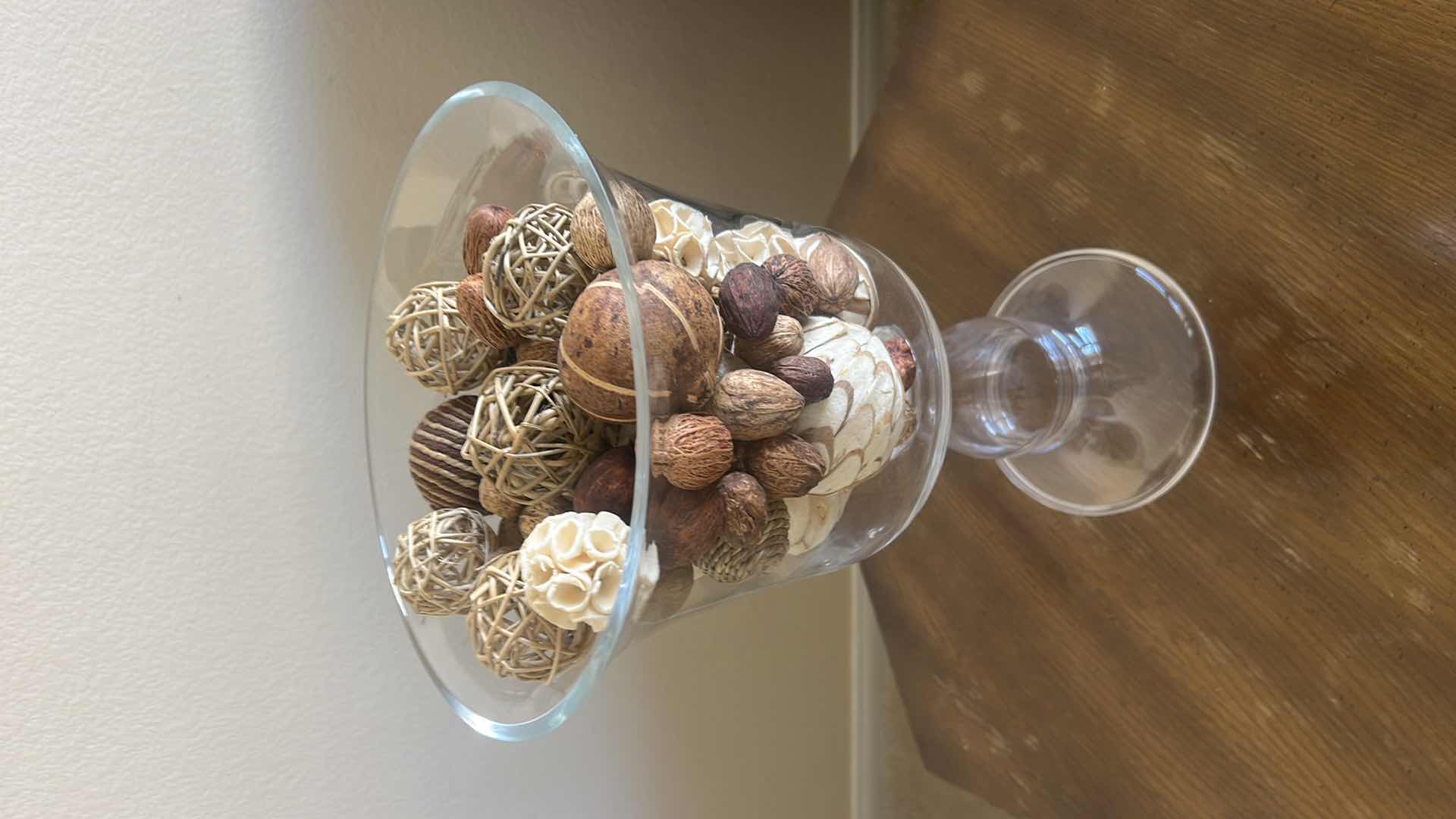 Photo 1 of CLEAR GLASS PEDESTAL VASE FILLED WITH DECORATIVE NATURAL BOTANICAL PODS AND ORBS.
H15”