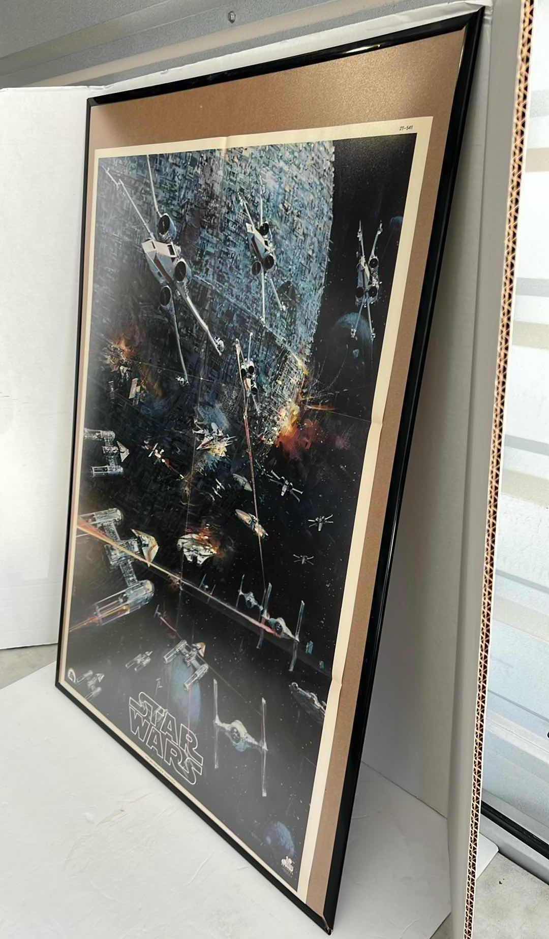 Photo 1 of STAR WARS MOVIE POSTER IN BLACK PLATIC FRAME(22.5”W X 32.5”H) AND STORM TROOPER HELMET HELMET SCHEMATIC IN DARK BROWN WOODEN FRAME(22.5”W X 19”H)