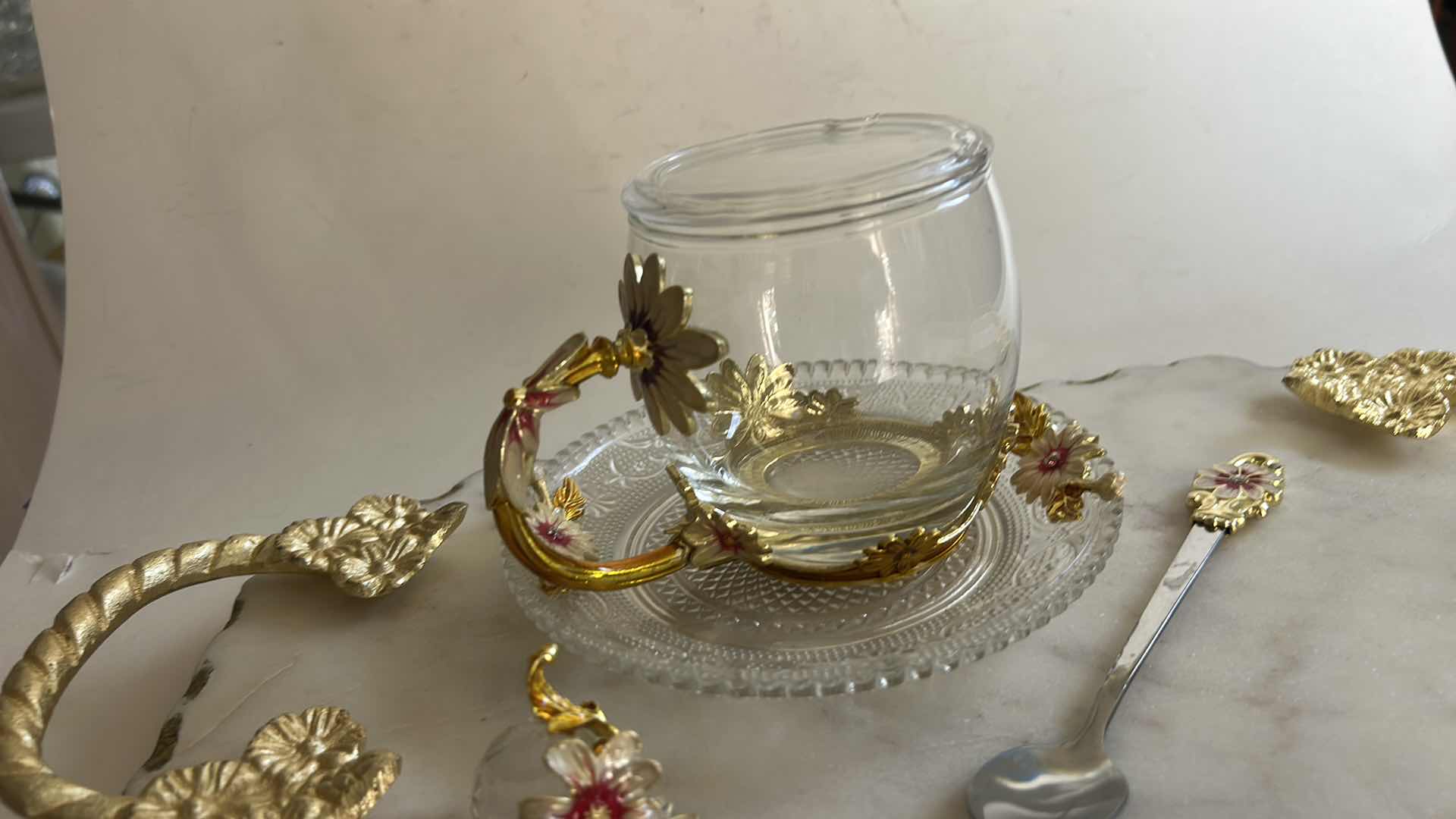 Photo 1 of VINTAGE-STYLE ENAMEL GLASS FLORAL TEA CUP FEATURES INTRICATE 3D BUTTERFLY AND ROSE DETAILS ON THE HANDLE AND LID & HANDMADE SERVING TRAY FEATURES A WHITE MARBLE BASE ACCENTED WITH INTRICATE GOLD-FINISHED METAL HANDLES.