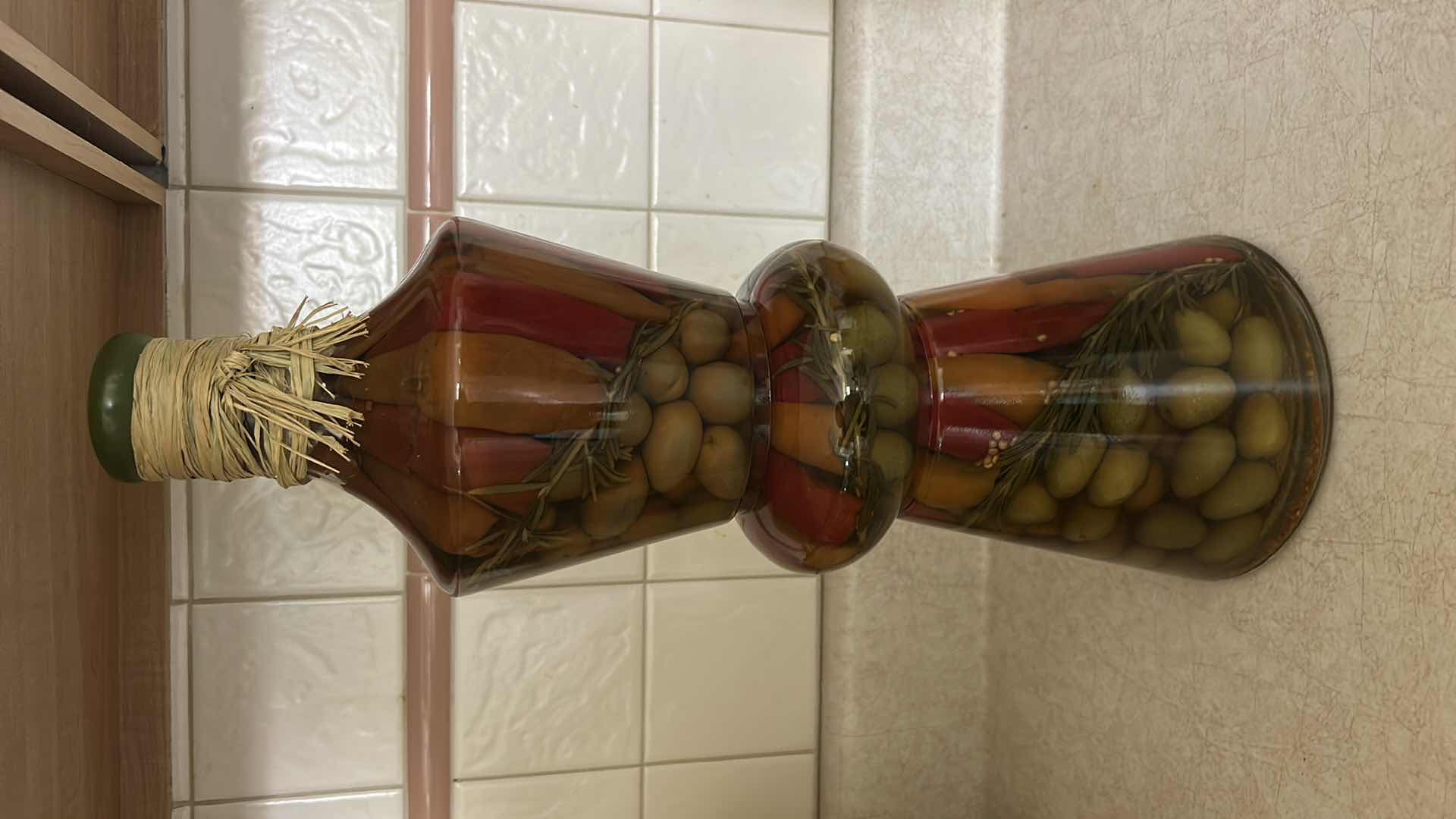 Photo 1 of DECORATIVE GLASS BOTTLE FEATURES STACKED LAYERS OF PRESERVED OLIVES, PEPPERS, AND HERBS. H17”