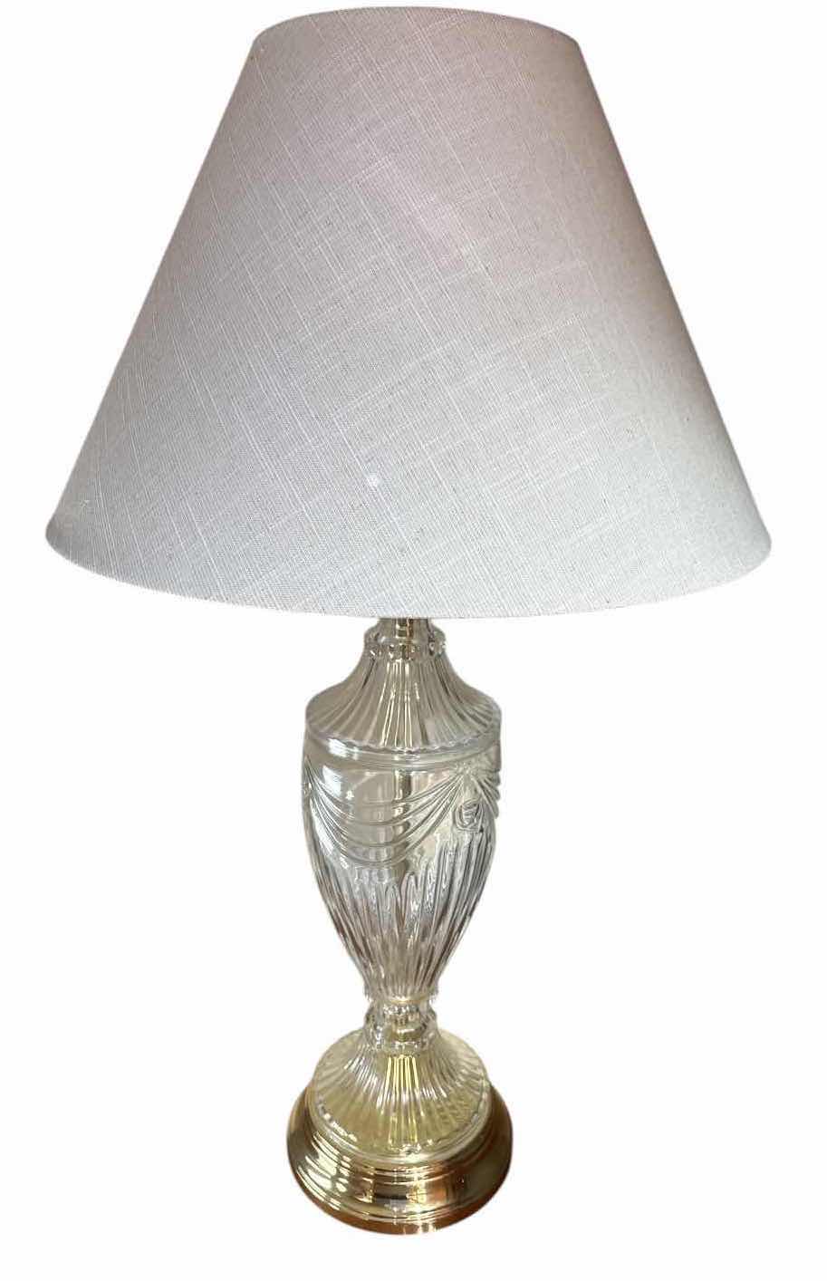 View 1 of CLEAR GLASS TABLE LAMP WITH GOLD TONE BASE & WHITE FABRIC SHADE H29” $60